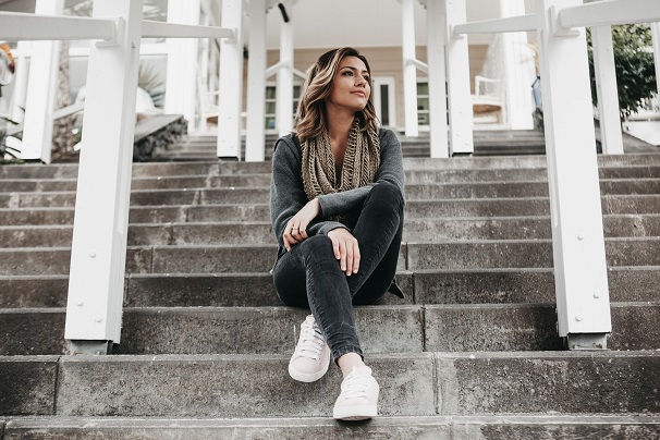 picture of woman sitting on concrete stairs wearing gray outfit and white sneakers