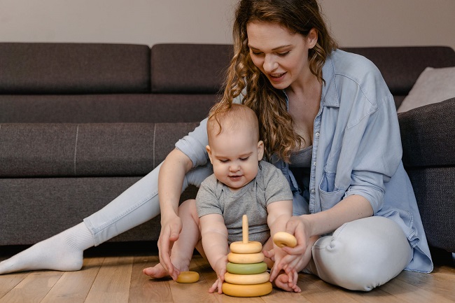picture of a woman beside a baby on a floor playing with a toy