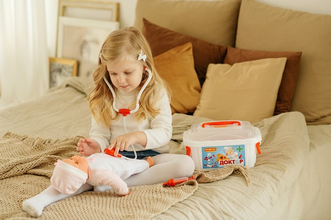 picture of a girl playing on a bed with a baby doll with doctor kit  