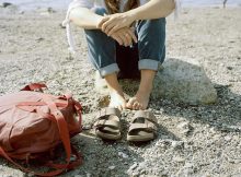picture of a woman sitting on the ground beside comfortable womens sandals and a bag