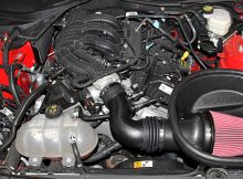 Upgraded air intake system with a red filter in a muscle car's engine bay.